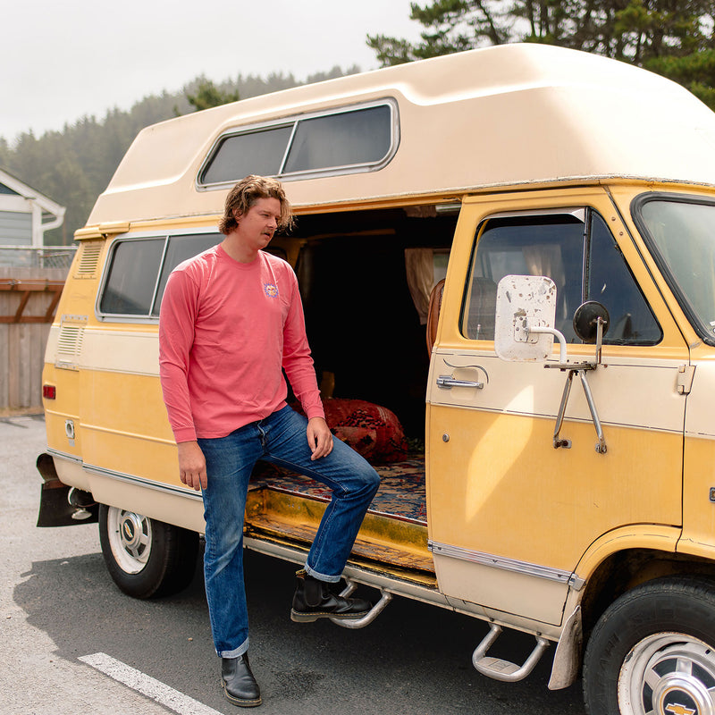 Load image into Gallery viewer, A man in the Sun Kissed Long Sleeve T-Shirt and blue jeans sits on the step of a vintage yellow and cream camper van parked outdoors.
