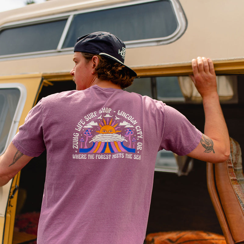 Load image into Gallery viewer, A man wearing the Where The Forest Meets The Sea T-Shirt with a colorful graphic on the back, standing next to a vintage camper van.
